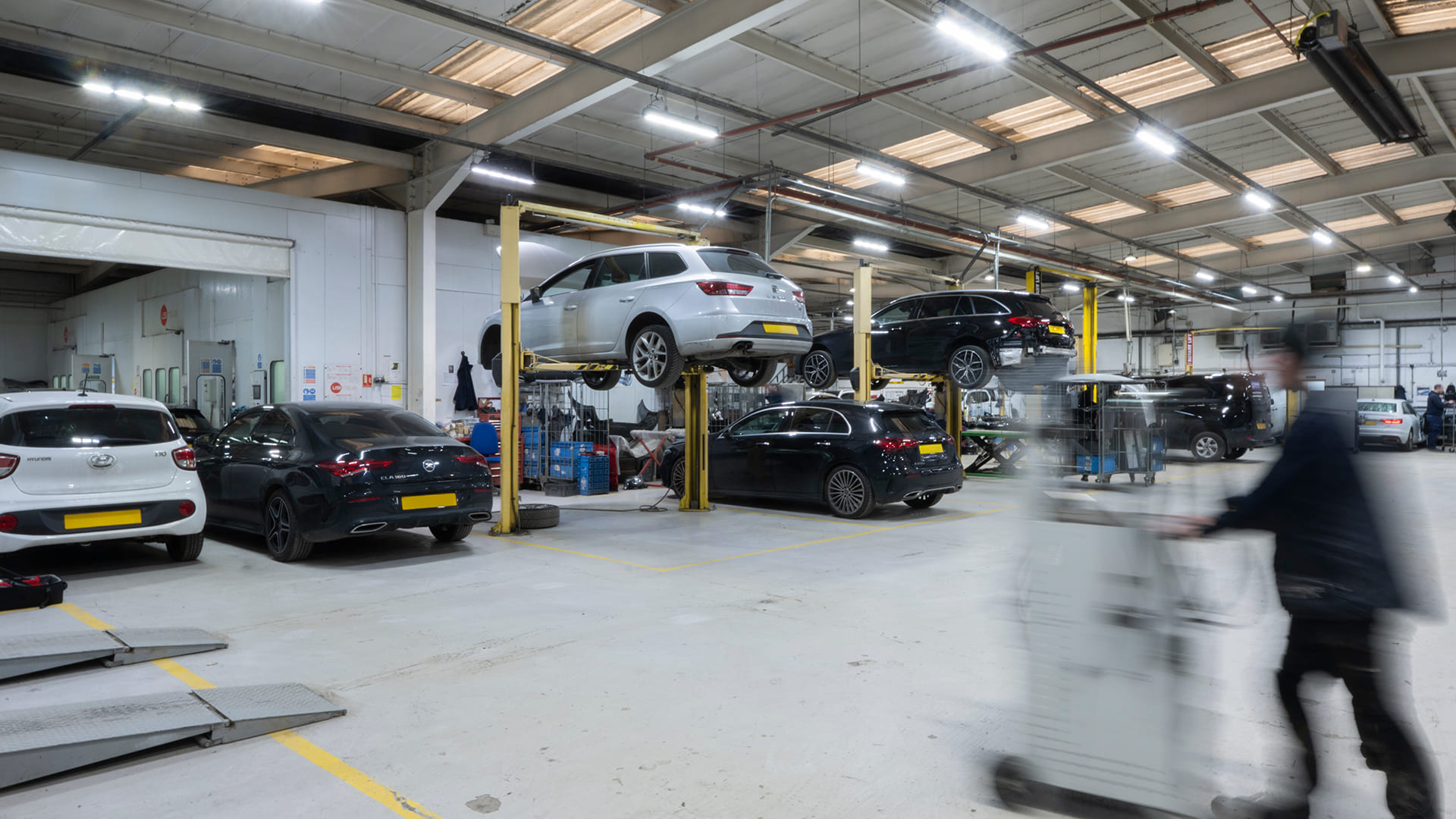 Blurred image of a modern car repair workshop with white cars on blue hydraulic lifts.