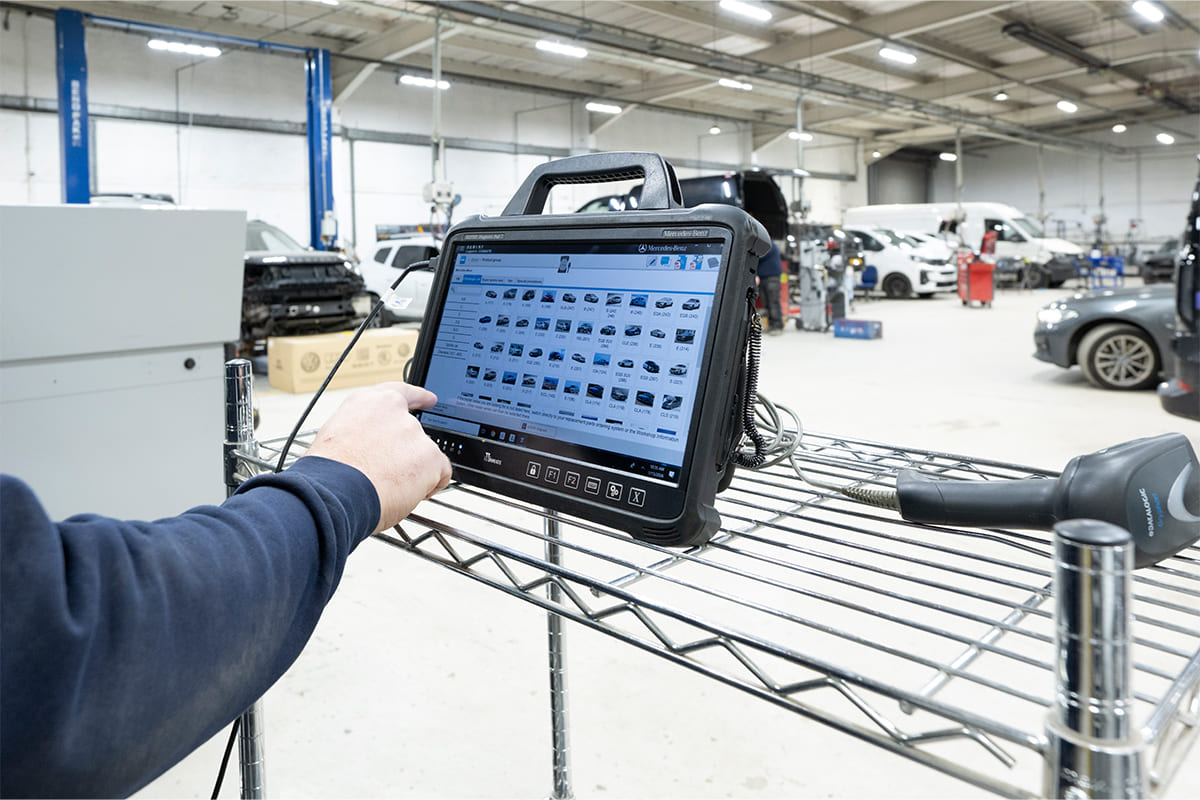 Technician using diagnostic equipment with car performance data displayed on a screen in a vehicle repair shop.