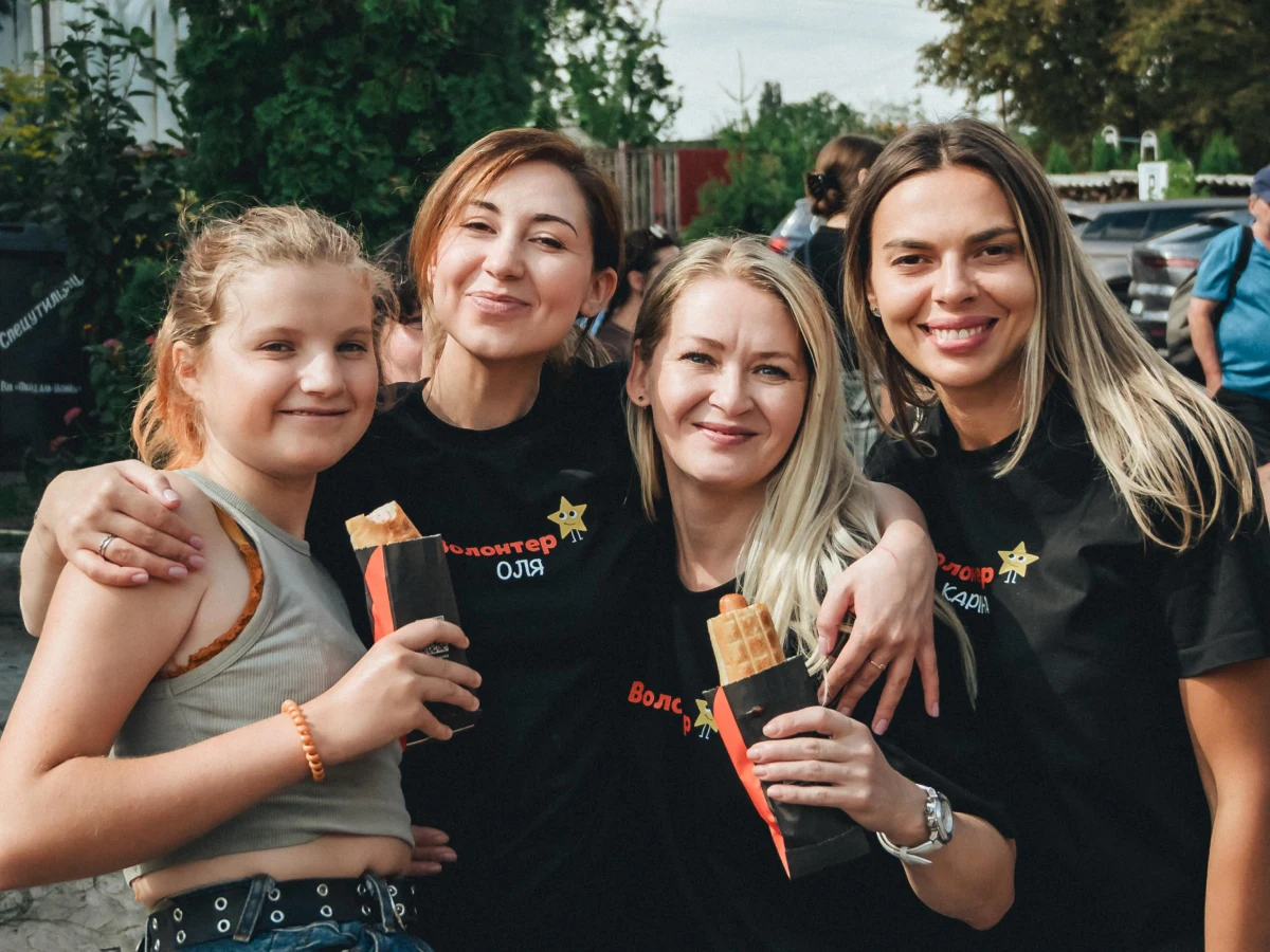 Волонтерки благодійного фонду разом із дитиною тримають смаколики під час заходу.