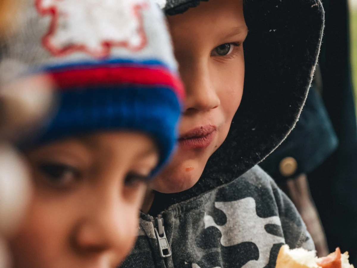 Двоє хлопчиків у теплому одязі їдять гарячу їжу під час благодійної акції на вулиці.