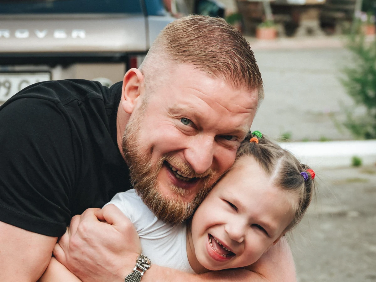 Волонтер обіймає дівчинку та усміхається під час благодійної події.