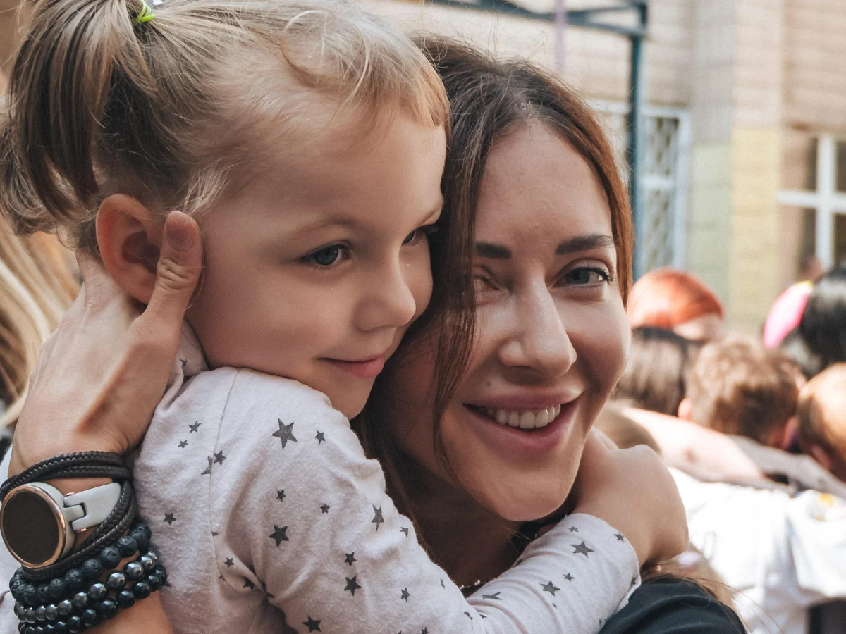 Волонтерка обіймає маленьку дівчинку під час благодійного заходу на подвір’ї.