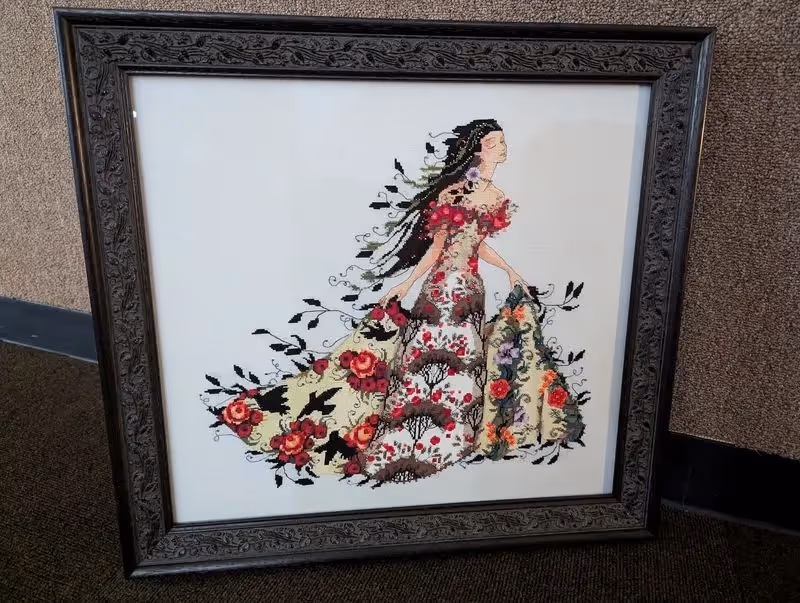 Framed embroidery artwork of a woman in a floral dress with flowing hair surrounded by intricate flower and leaf patterns.