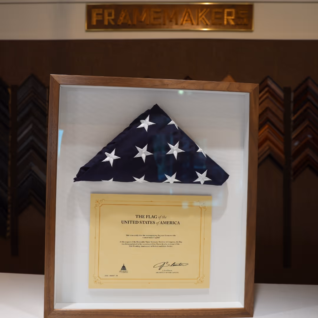 Folded American flag in a wooden display case with a certificate beneath it.