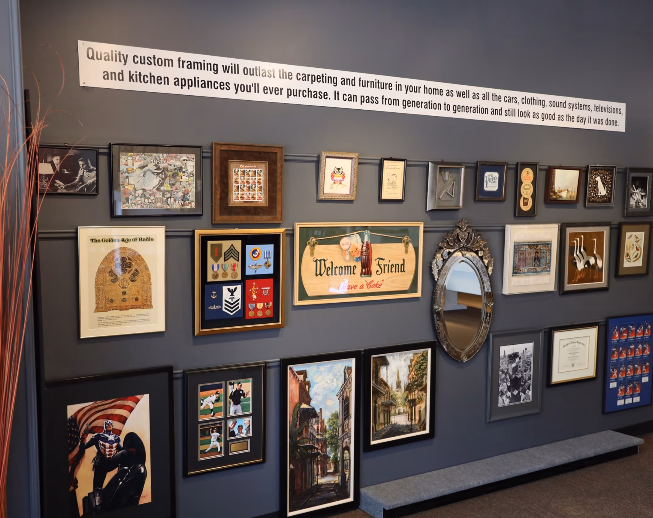 Wall display of various framed artworks, memorabilia, and a decorative mirror beneath a banner about custom framing quality.