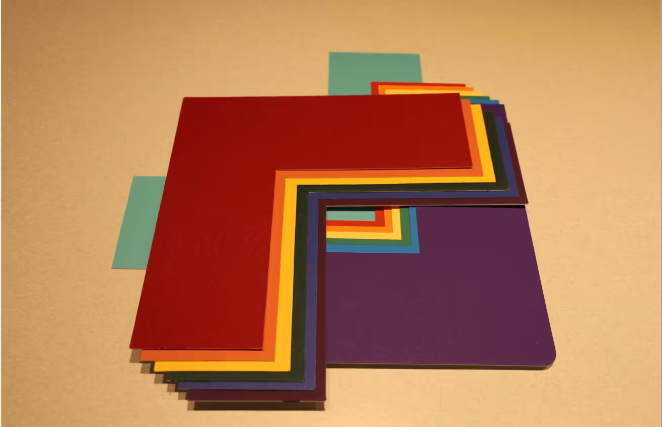 Stack of colorful L-shaped mat boards arranged in layers on a beige surface.