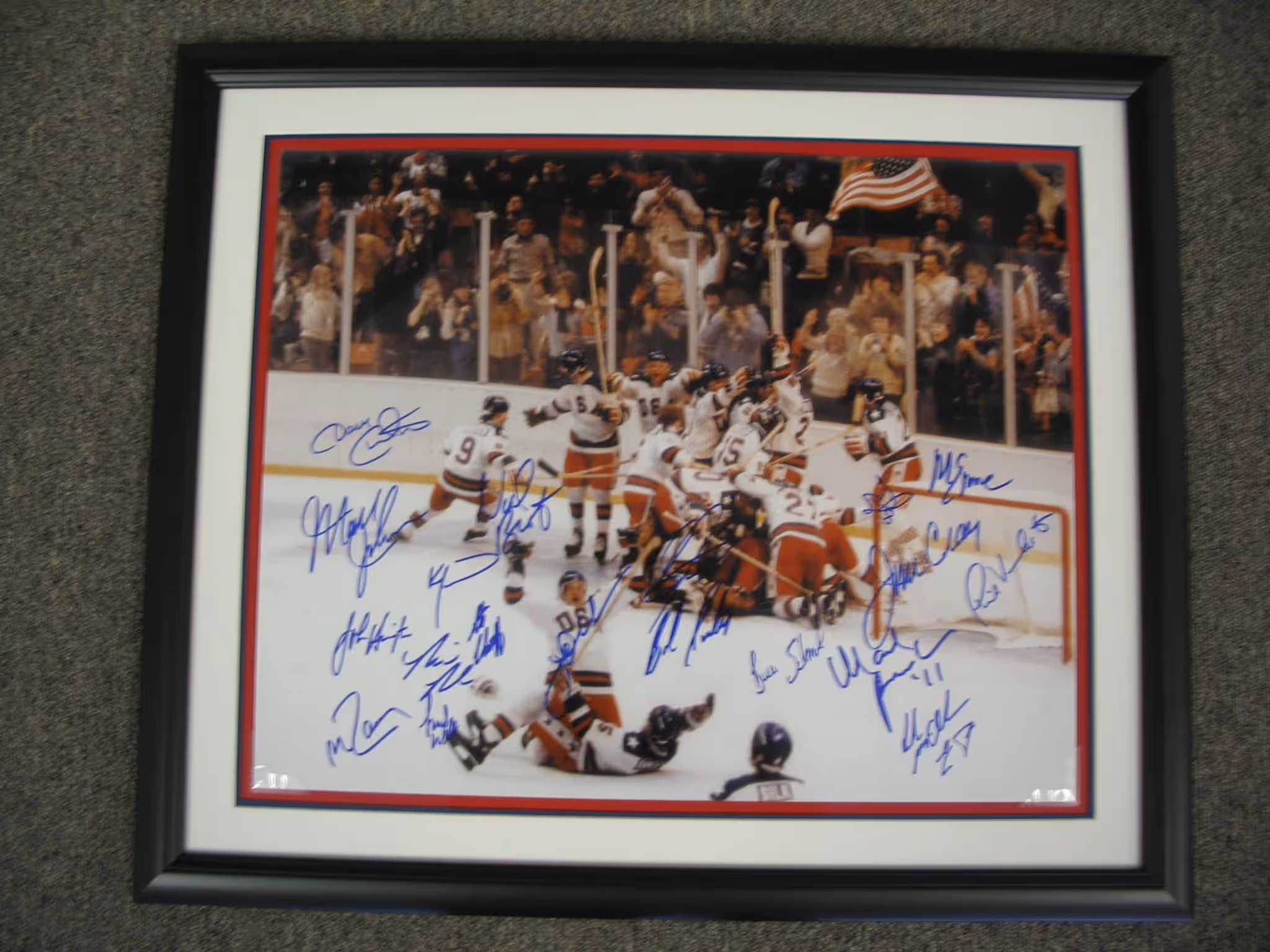 Framed and autographed photo of a hockey team celebrating on ice with an American flag in the background and cheering crowd.
