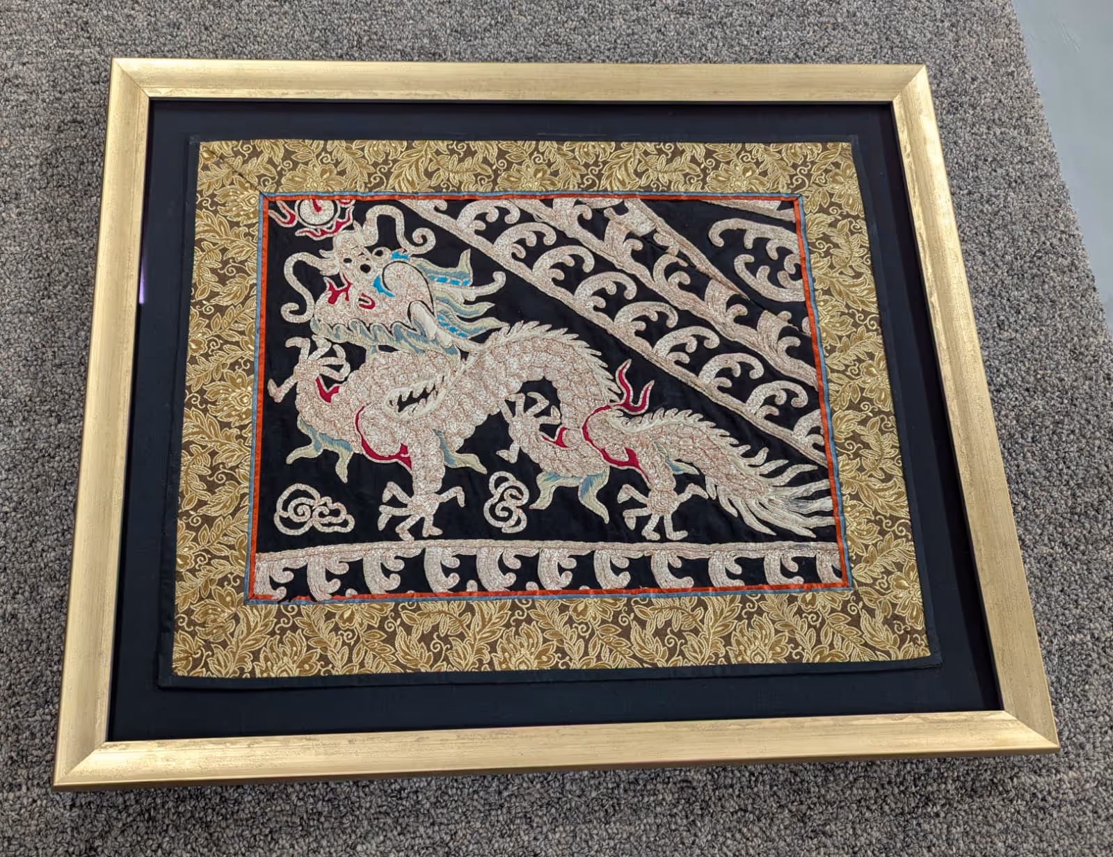 Framed textile artwork featuring an embroidered white Chinese dragon on a black background with gold and floral patterned borders.
