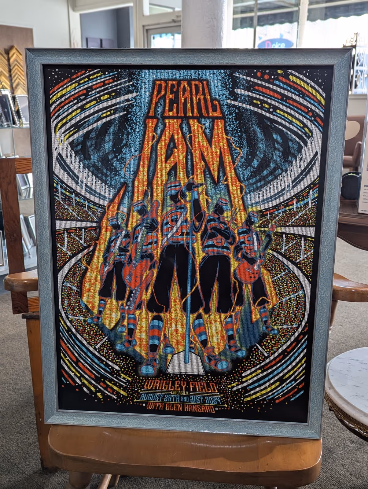 Framed Pearl Jam concert poster featuring illustrated band members in striped outfits surrounded by flames and an abstract stadium background, with text referencing Wrigley Field, Chicago, and dates August 29th and 31st, 2023, with Glen Hansard.