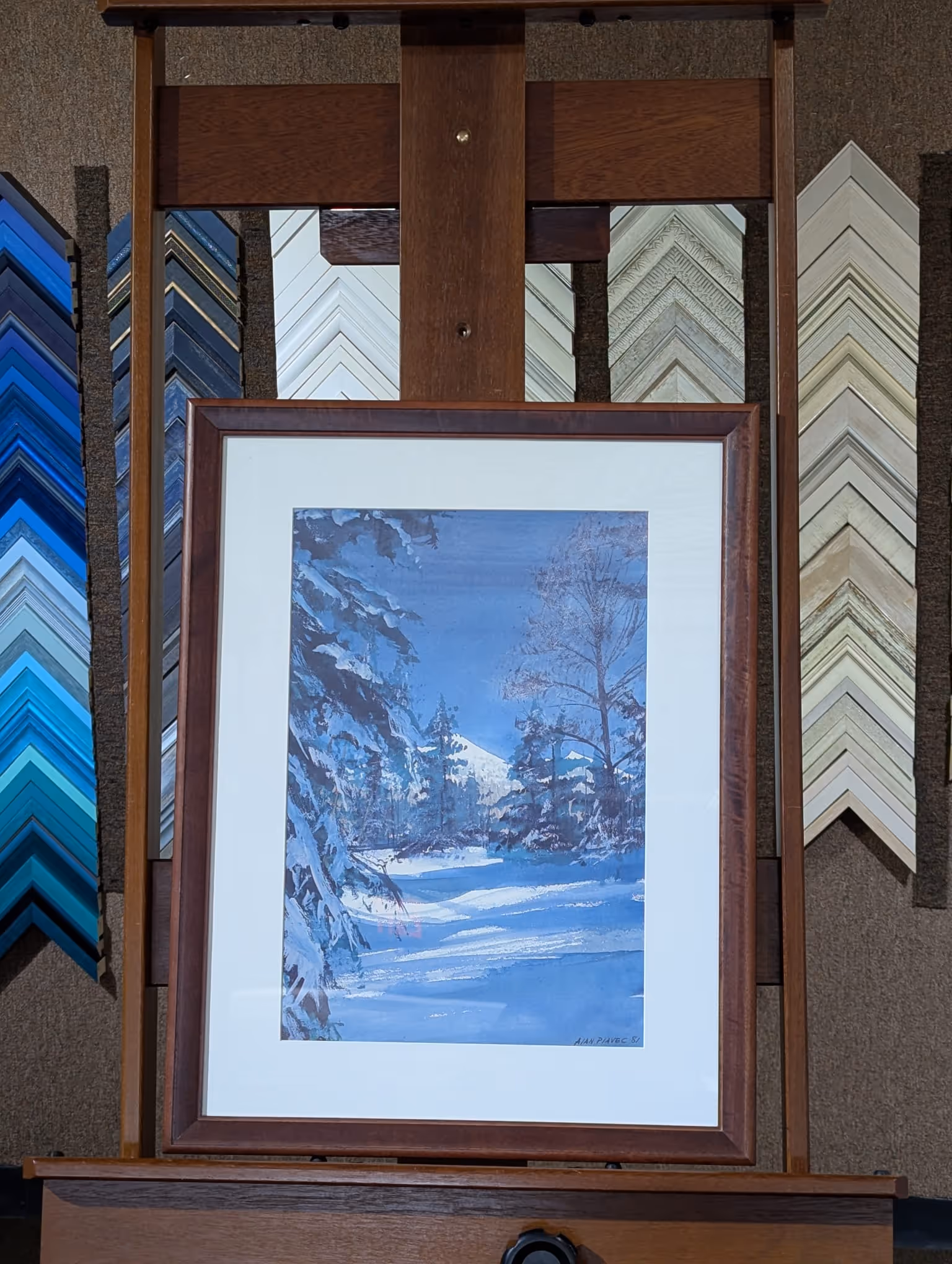 Framed painting of a snowy winter landscape with snow-covered trees and a distant snowy mountain under a clear blue sky.