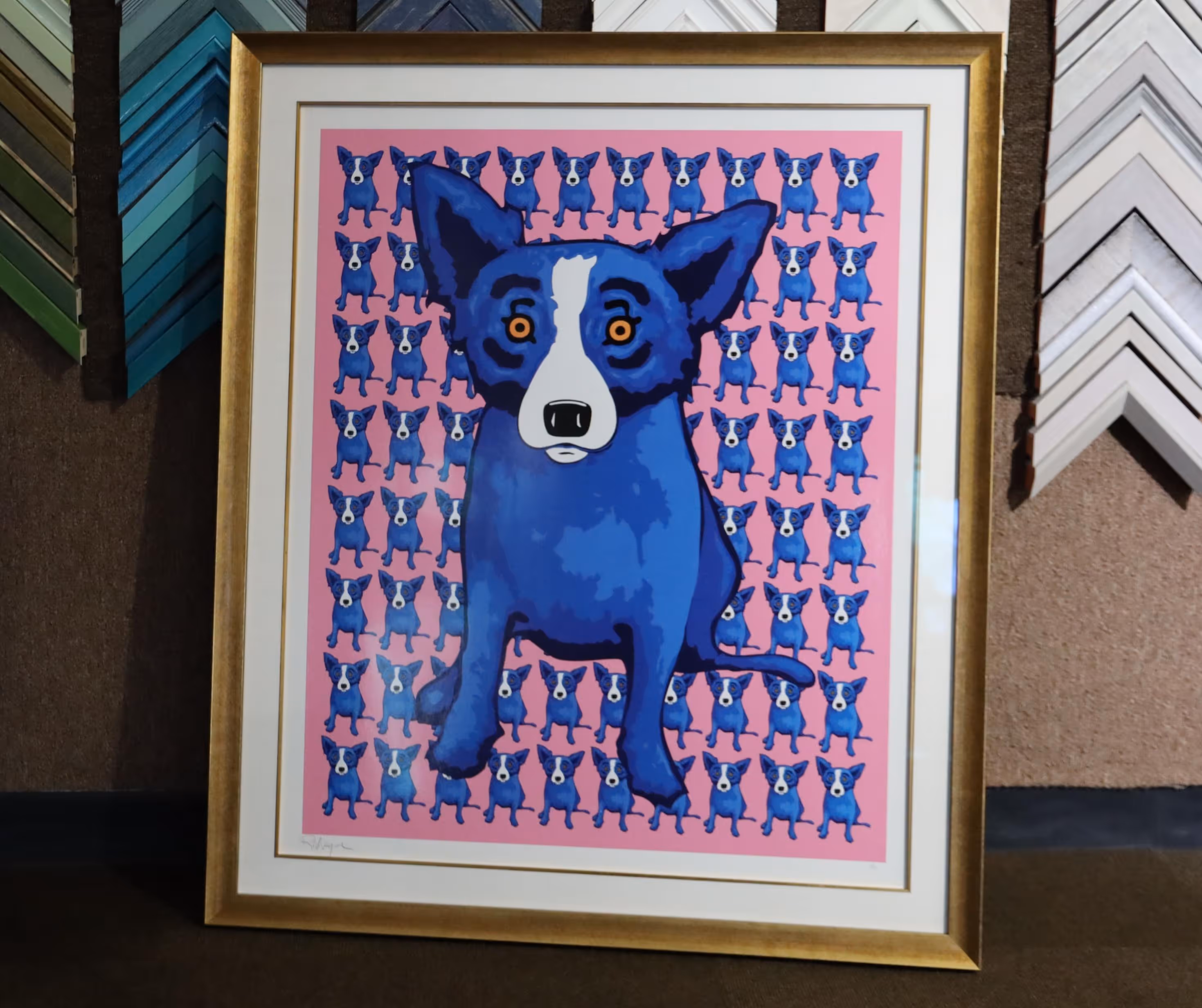 Framed artwork of a large blue dog with orange eyes on a pink background filled with smaller blue dogs.