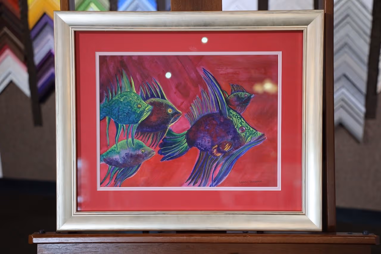 Framed colorful painting of five stylized fish with green, purple, and blue hues on a red background.