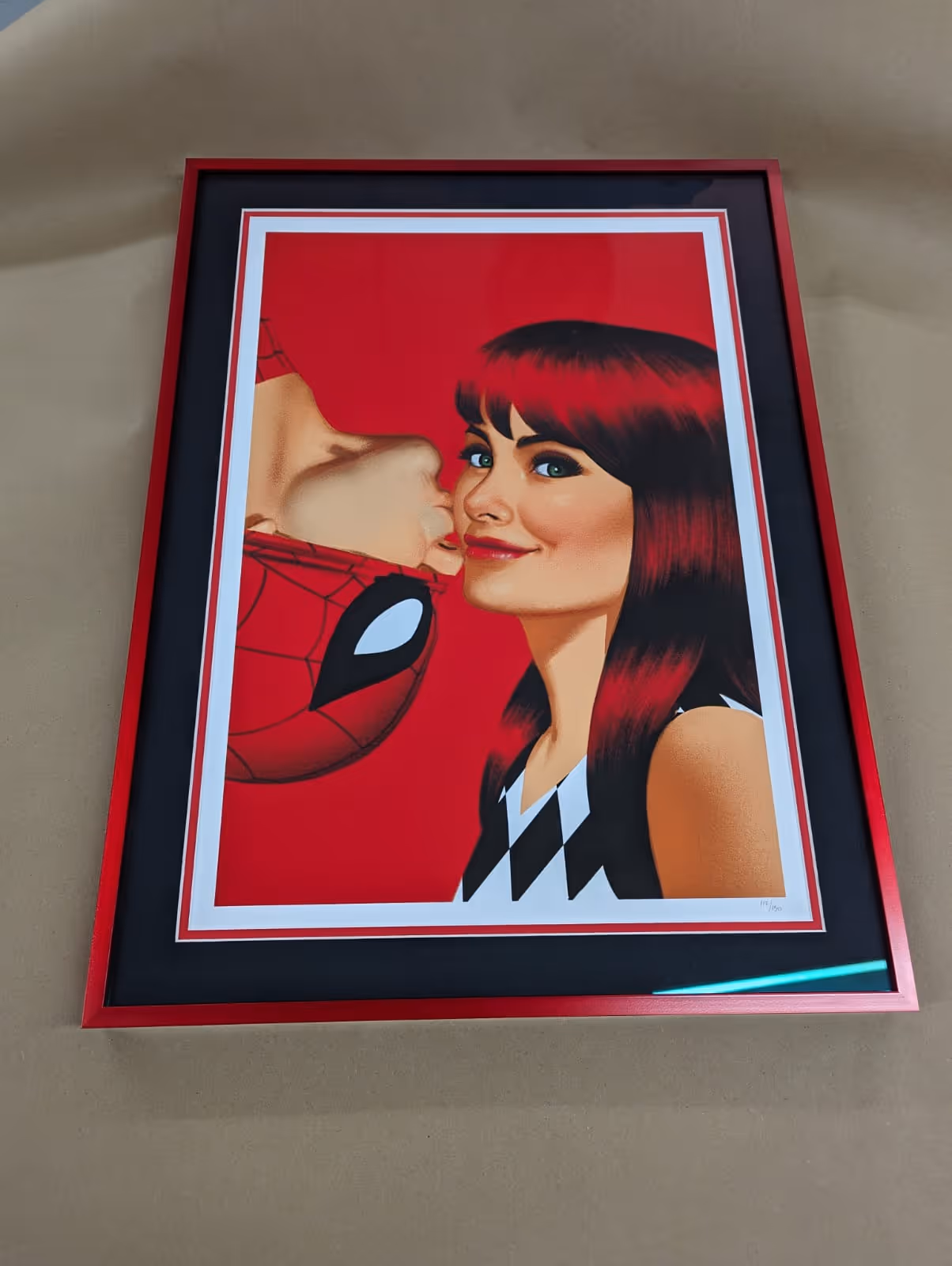 Framed artwork of Spider-Man kissing Mary Jane Watson on the cheek with a red background.