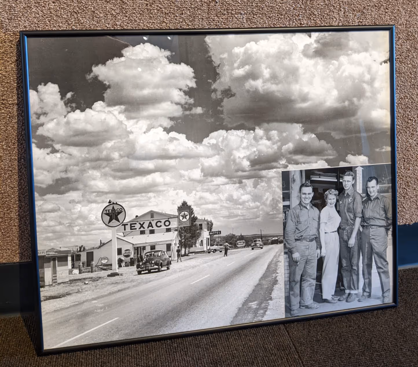 Framed black and white photo of a vintage Texaco gas station on a road under a cloudy sky, with an inset photo of four people standing and smiling.