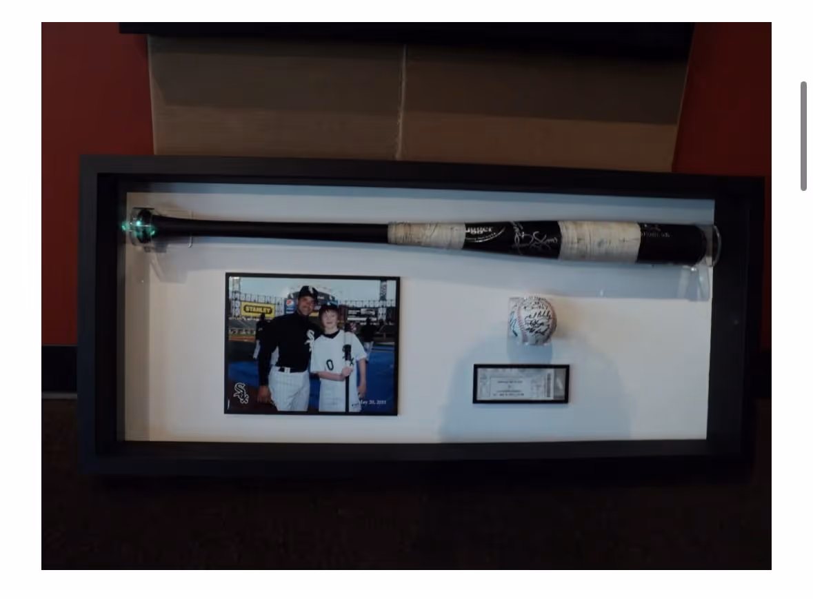 Framed display case containing a signed baseball bat, a photo of two people in White Sox uniforms, a signed baseball, and a plaque.