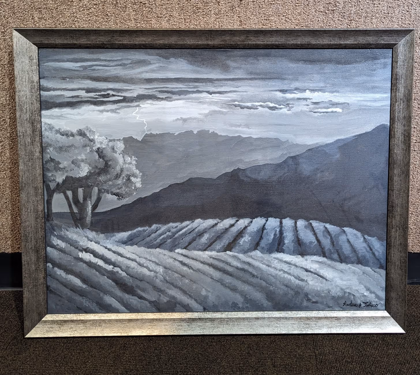 Framed grayscale painting of a landscape with cultivated fields, trees, mountain layers, cloudy sky, and a lightning bolt.