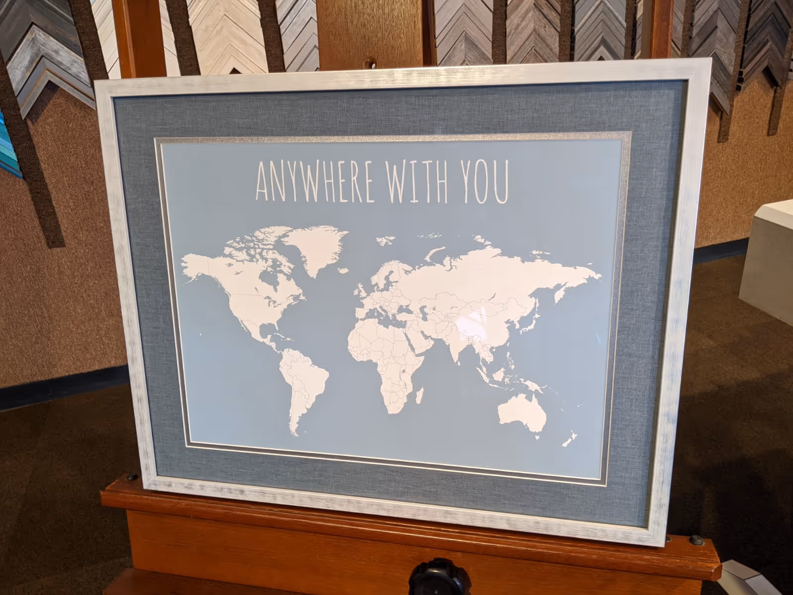 Framed world map with countries outlined and text above reading 'ANYWHERE WITH YOU' on blue background.