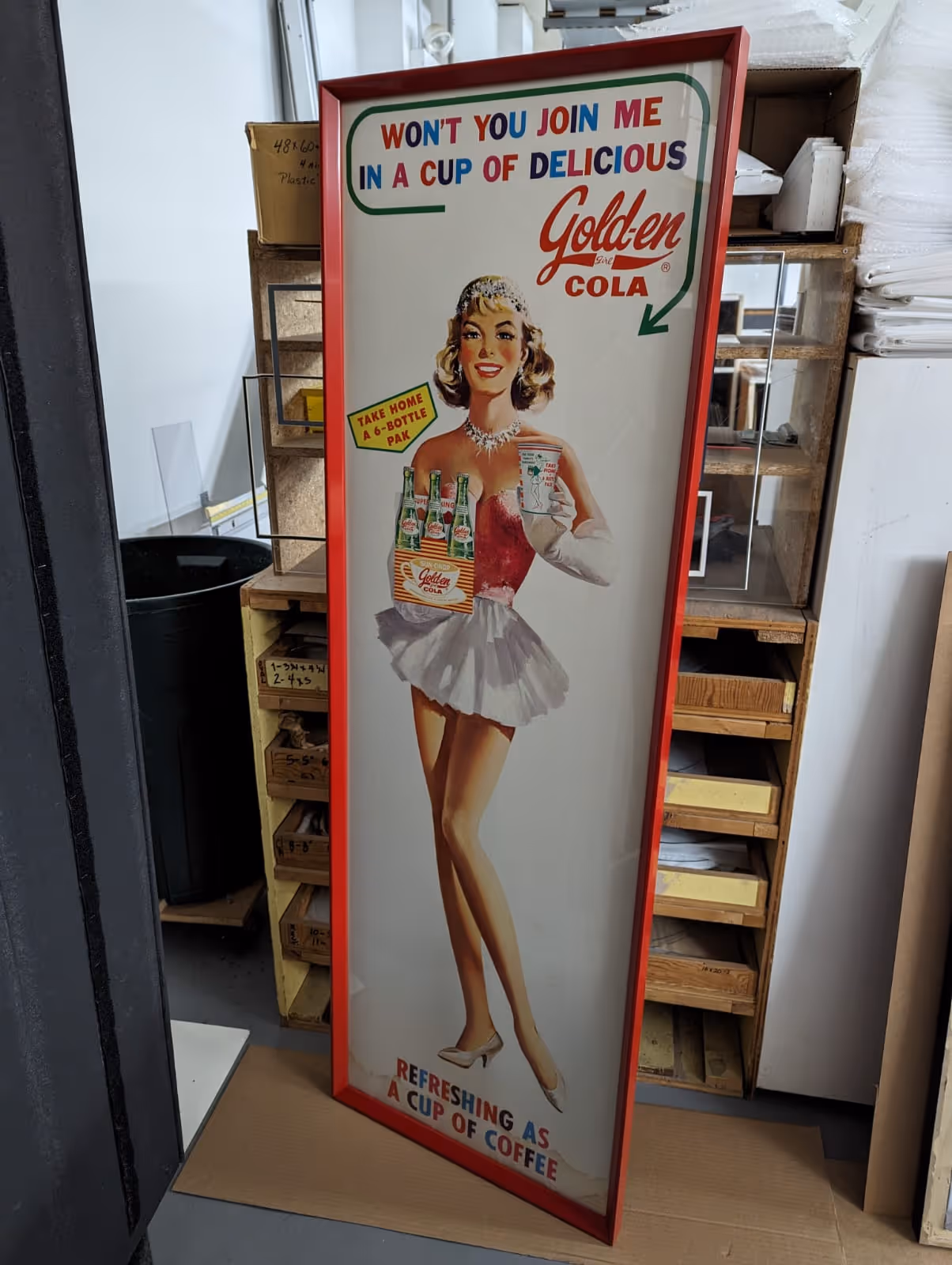 Vintage advertisement poster of a smiling woman in a red top and white skirt holding a pack of Golden Cola bottles and a cup.