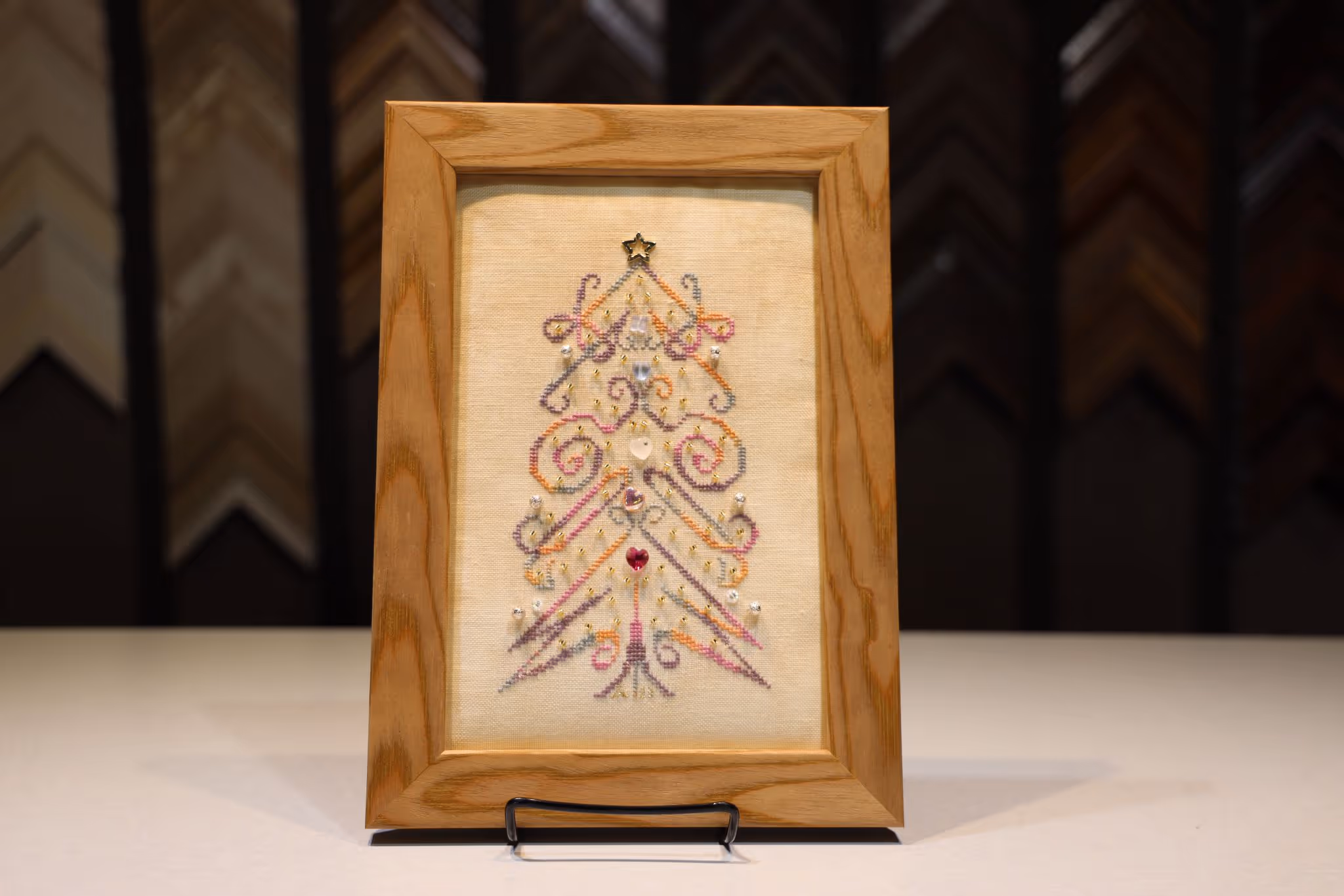 Framed embroidery of a Christmas tree decorated with colorful swirls and small jeweled embellishments.