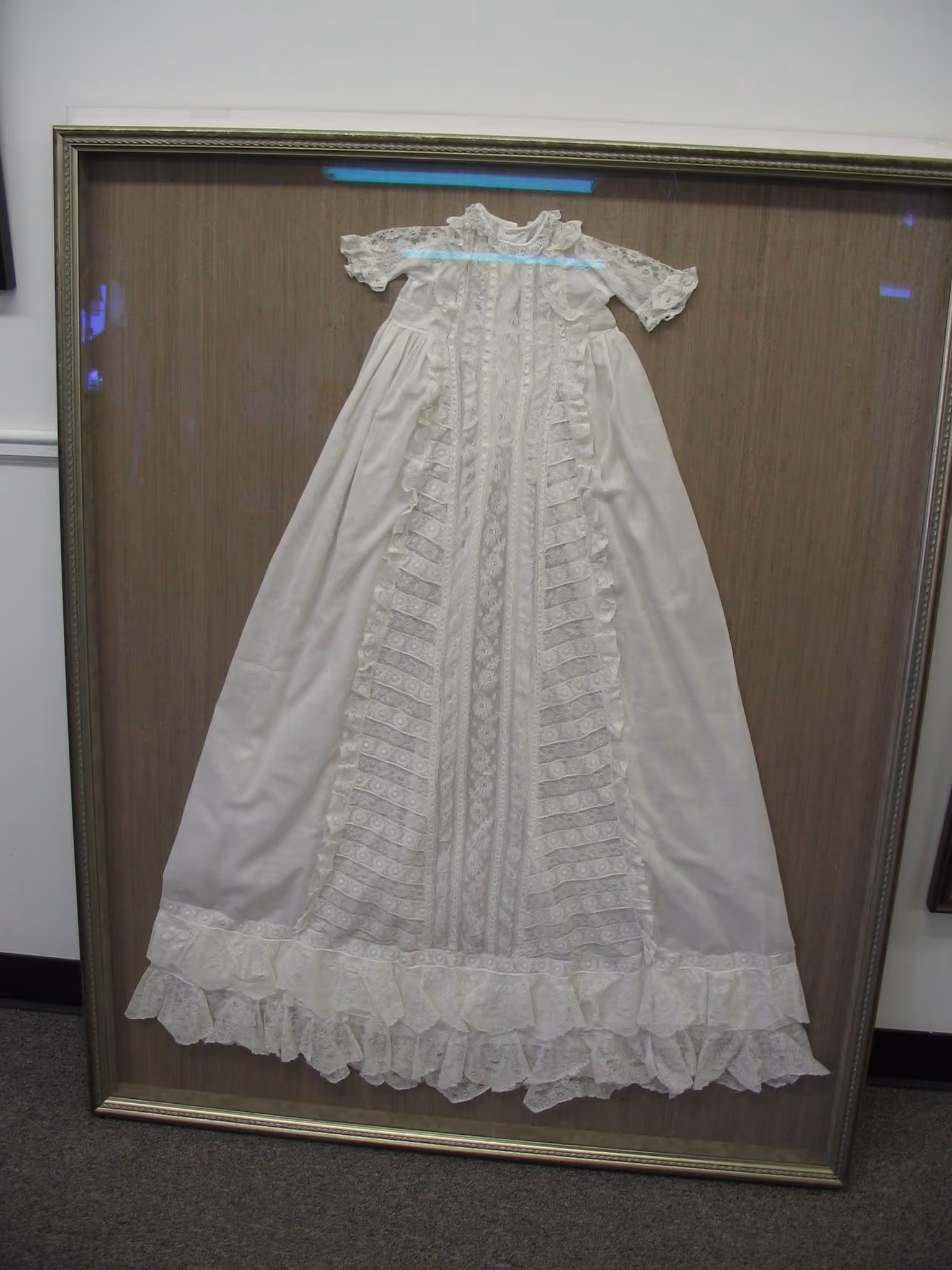 Framed vintage white lace baby dress with puffed sleeves and ruffled trim on the bottom.