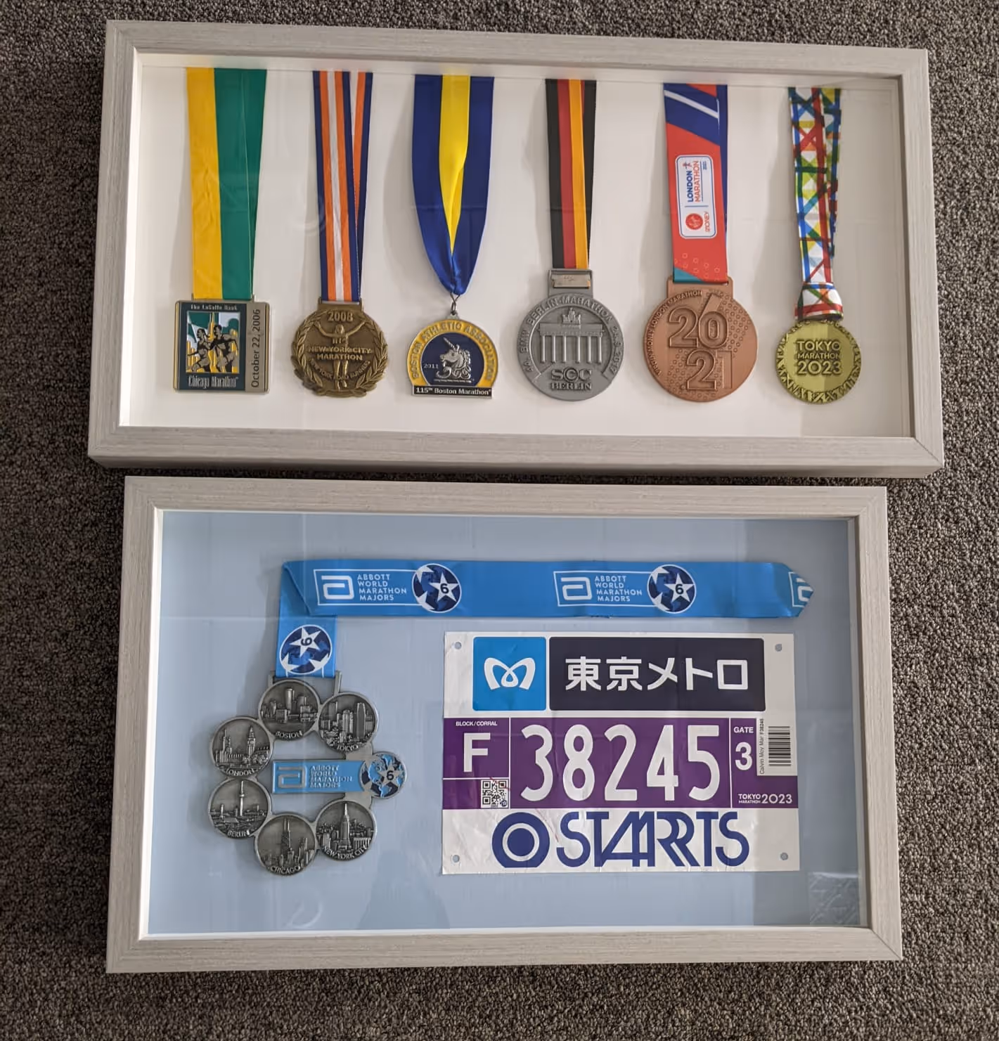 Two framed displays of marathon memorabilia: upper frame holds seven marathon medals from 2006 to 2023; lower frame contains a medal with skyline engravings and a blue race bib numbered 38245 for Tokyo Marathon 2023.