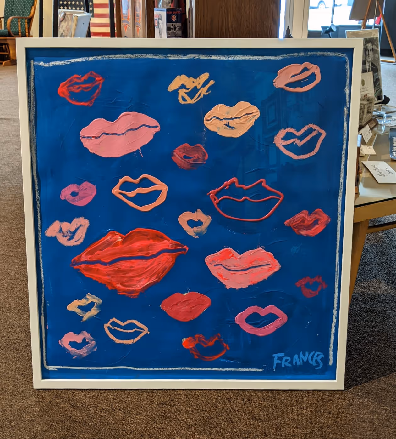 Painting featuring various abstract lips in red, pink, peach, and orange on a blue background, signed 'FRANCE' in bottom right.