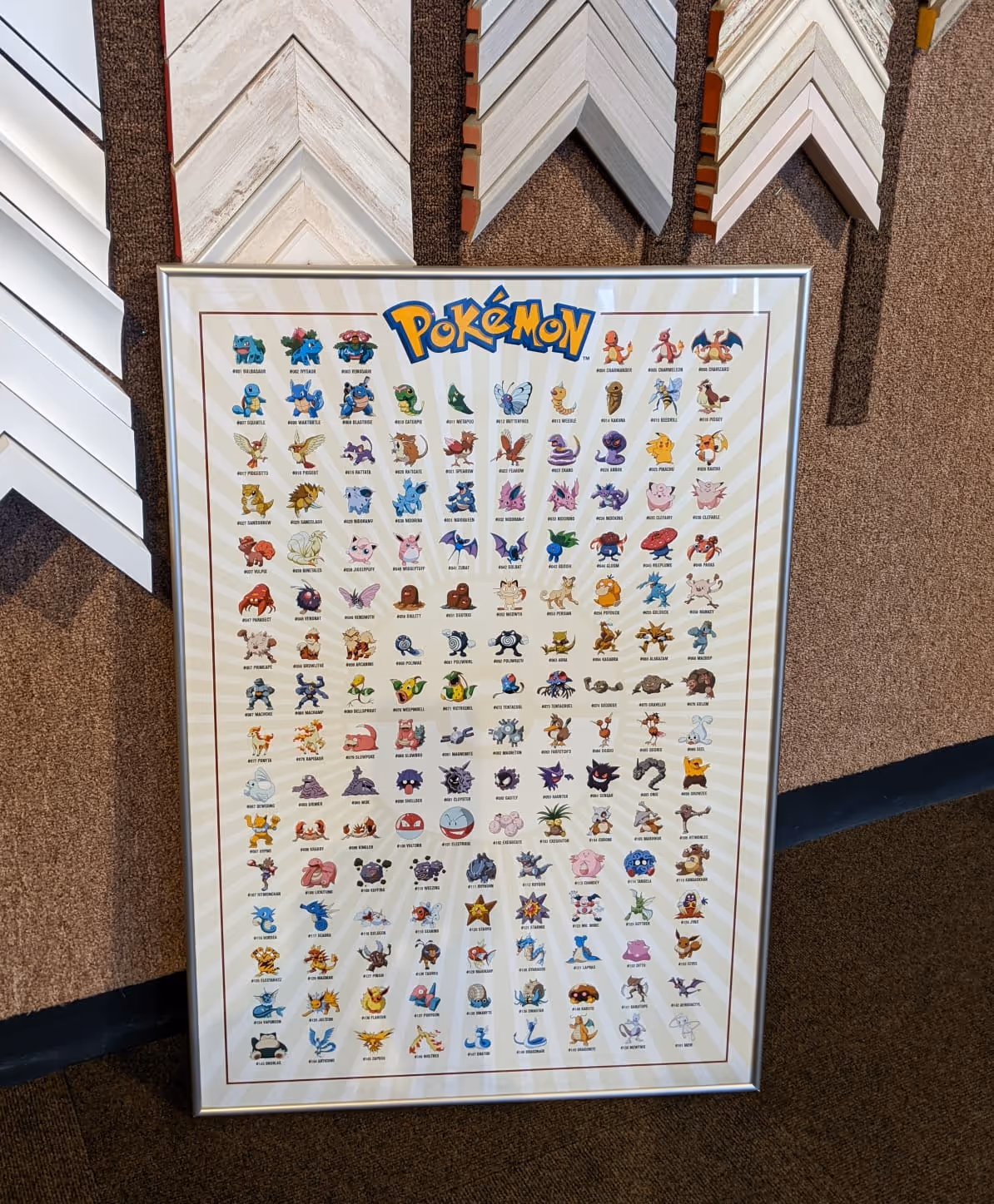 Framed poster showing original 151 Pokémon characters with names and numbers, displayed against a beige background.