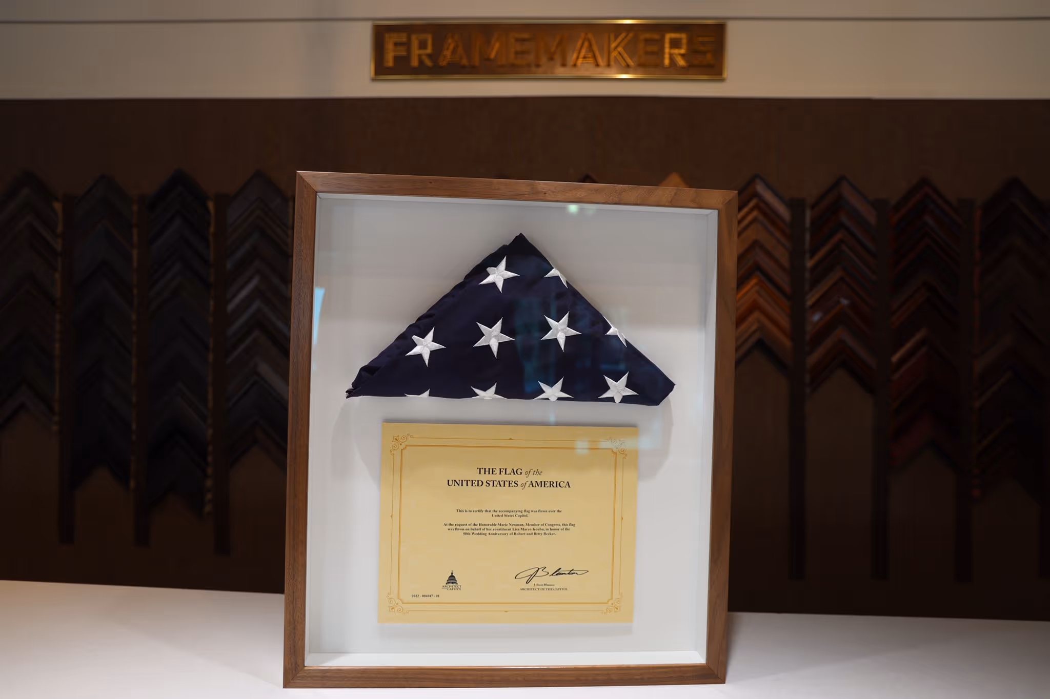 Folded United States flag in a wooden frame with a certificate beneath it.