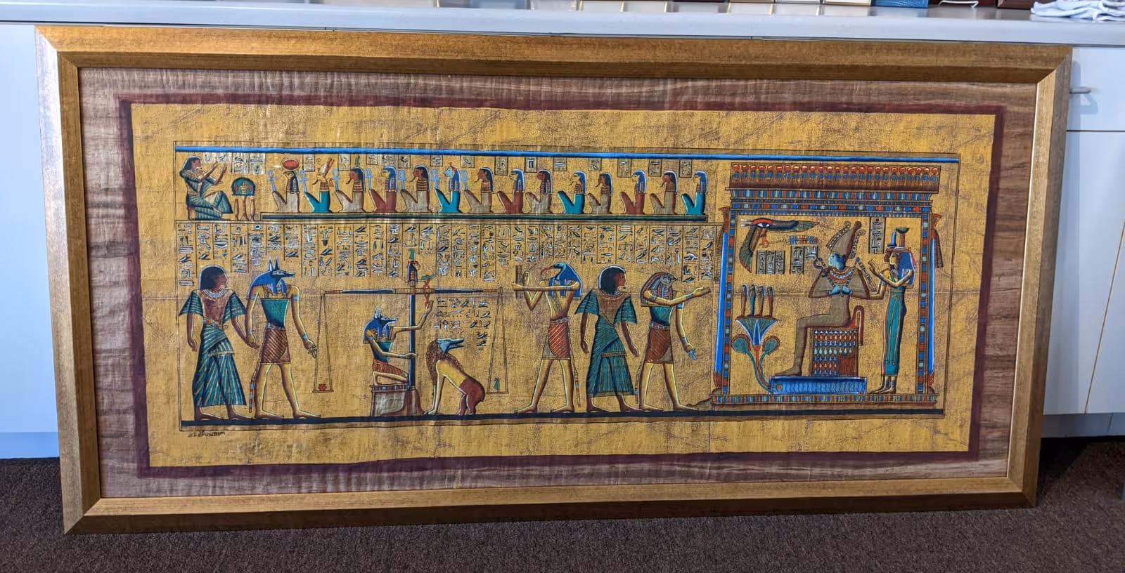Framed ancient Egyptian papyrus painting depicting gods, hieroglyphics, and a scene of weighing a heart against a feather.
