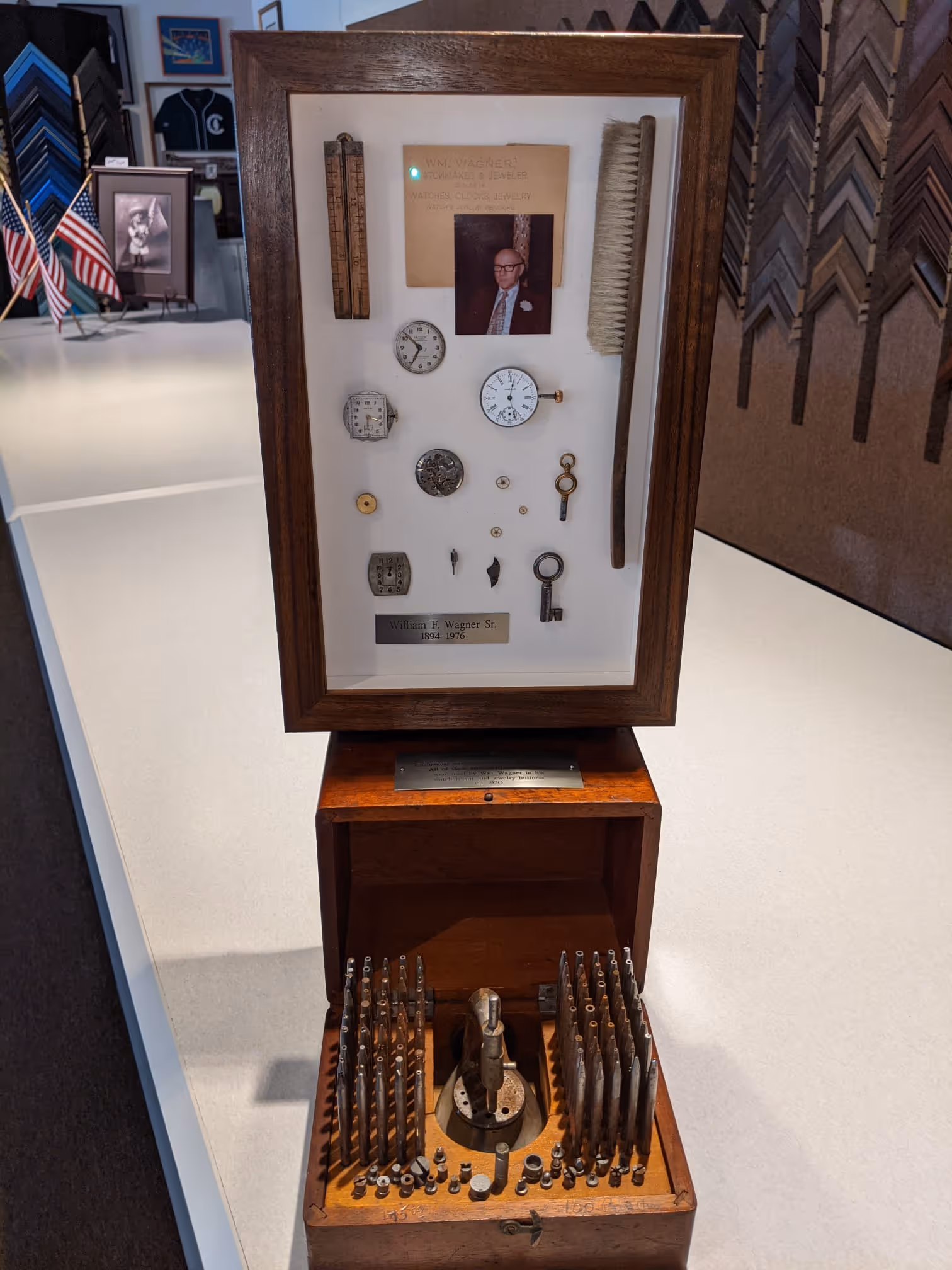 Wooden display case containing watch parts, keys, and a photo of William F. Wagner Sr., with tools arranged in an open wooden box beneath it.