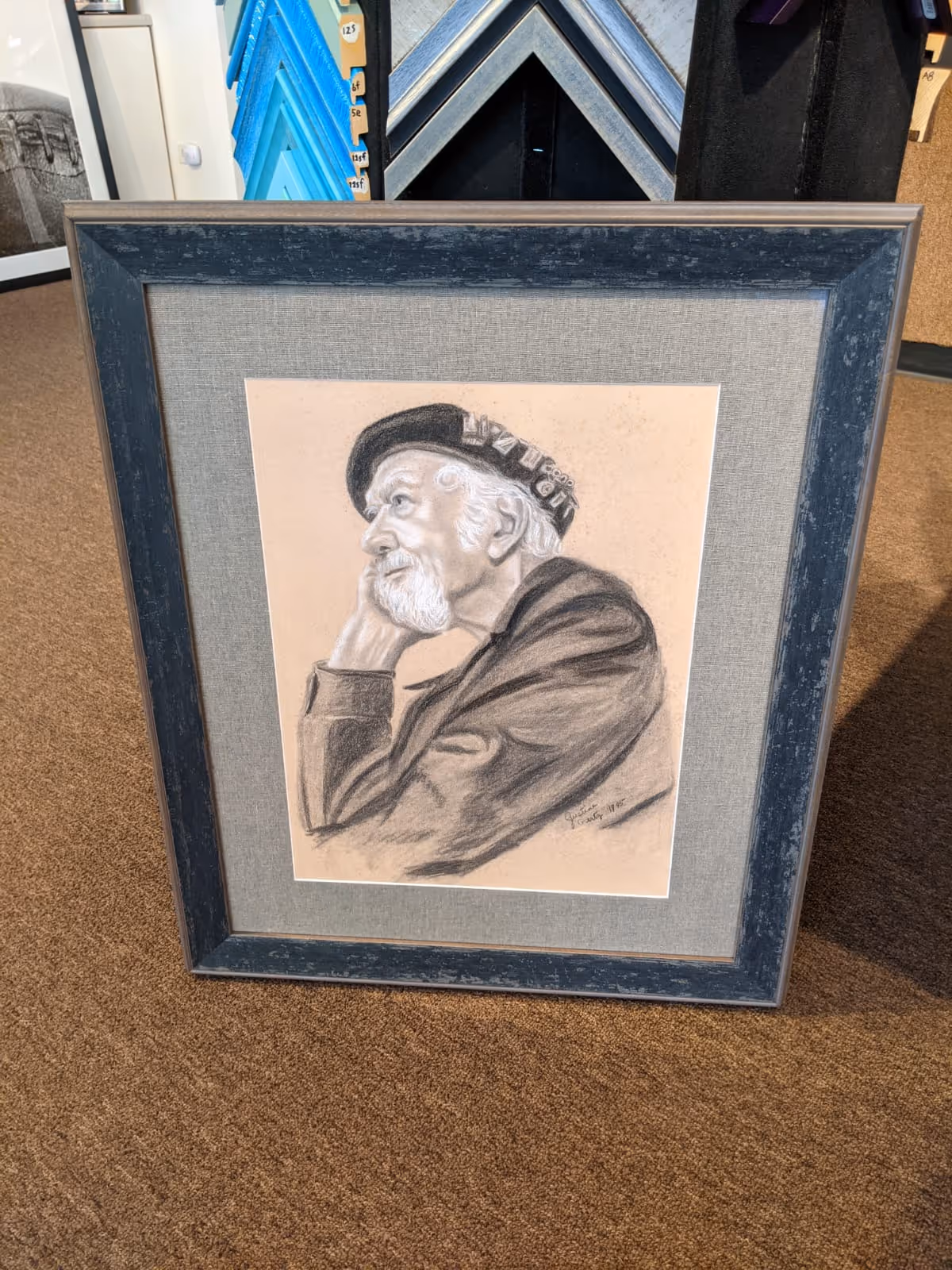 Framed charcoal sketch of an elderly man with a white beard, wearing a beret and resting his head on his hand, looking contemplative.