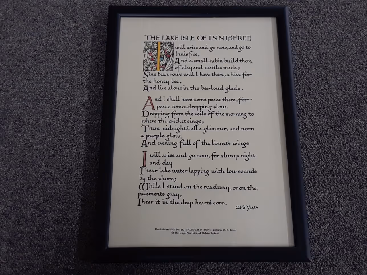 Framed calligraphy print of the poem 'The Lake Isle of Innisfree' by W.B. Yeats displayed on a gray carpet.
