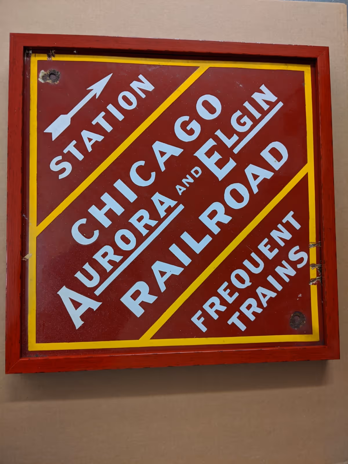 Vintage red and yellow Chicago Aurora and Elgin Railroad sign with white text and an arrow indicating station with frequent trains.