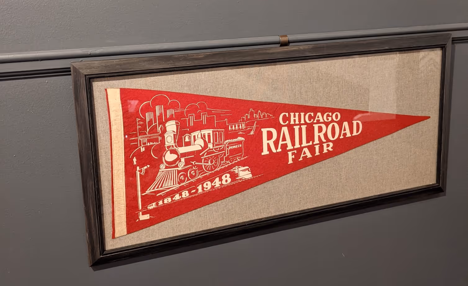 Framed red pennant with white illustration of a steam locomotive and Chicago skyline, labeled Chicago Railroad Fair 1848-1948.