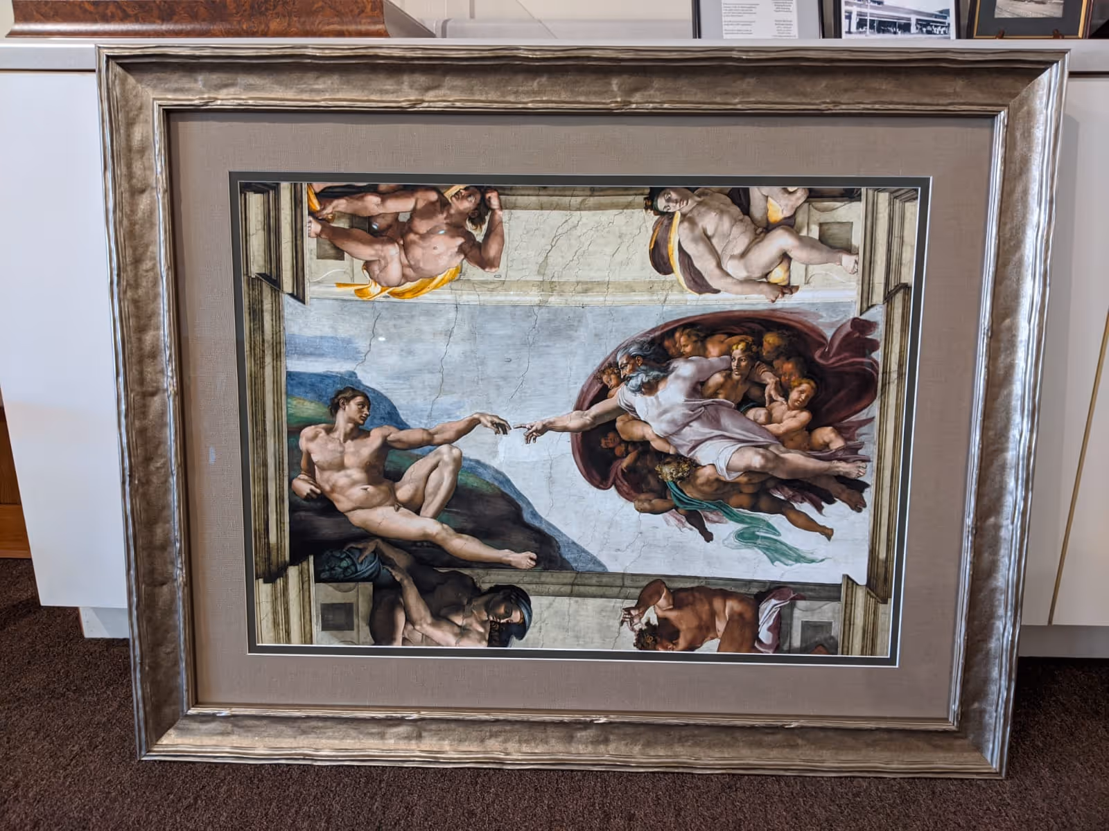 Framed painting of Michelangelo's The Creation of Adam depicting God and Adam reaching their hands toward each other.