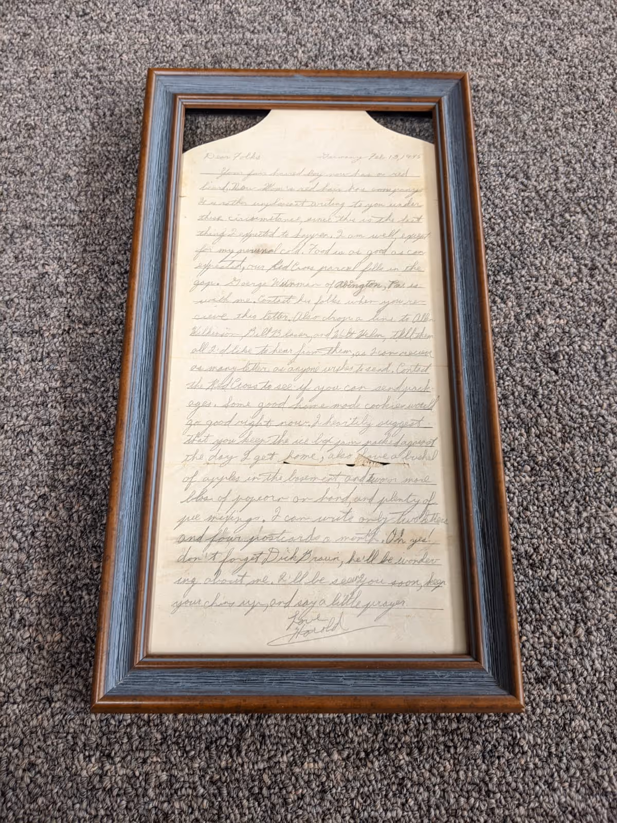 Framed, handwritten letter on beige paper with cursive writing, displayed on gray carpet.