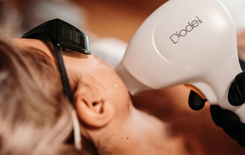 Nahaufnahme: Person mit Schutzbrille erhält Diodenlaser-Behandlung am Kiefer von behandschuhter Fachperson.