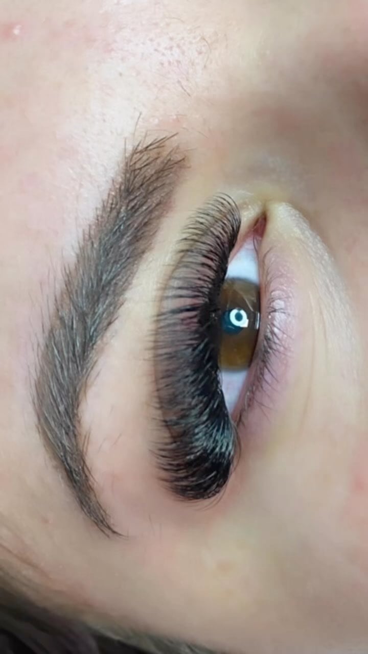 Nahaufnahme eines braunen Auges mit langen, dichten Wimpernextensions und einer gutdefinierten Augenbraue.