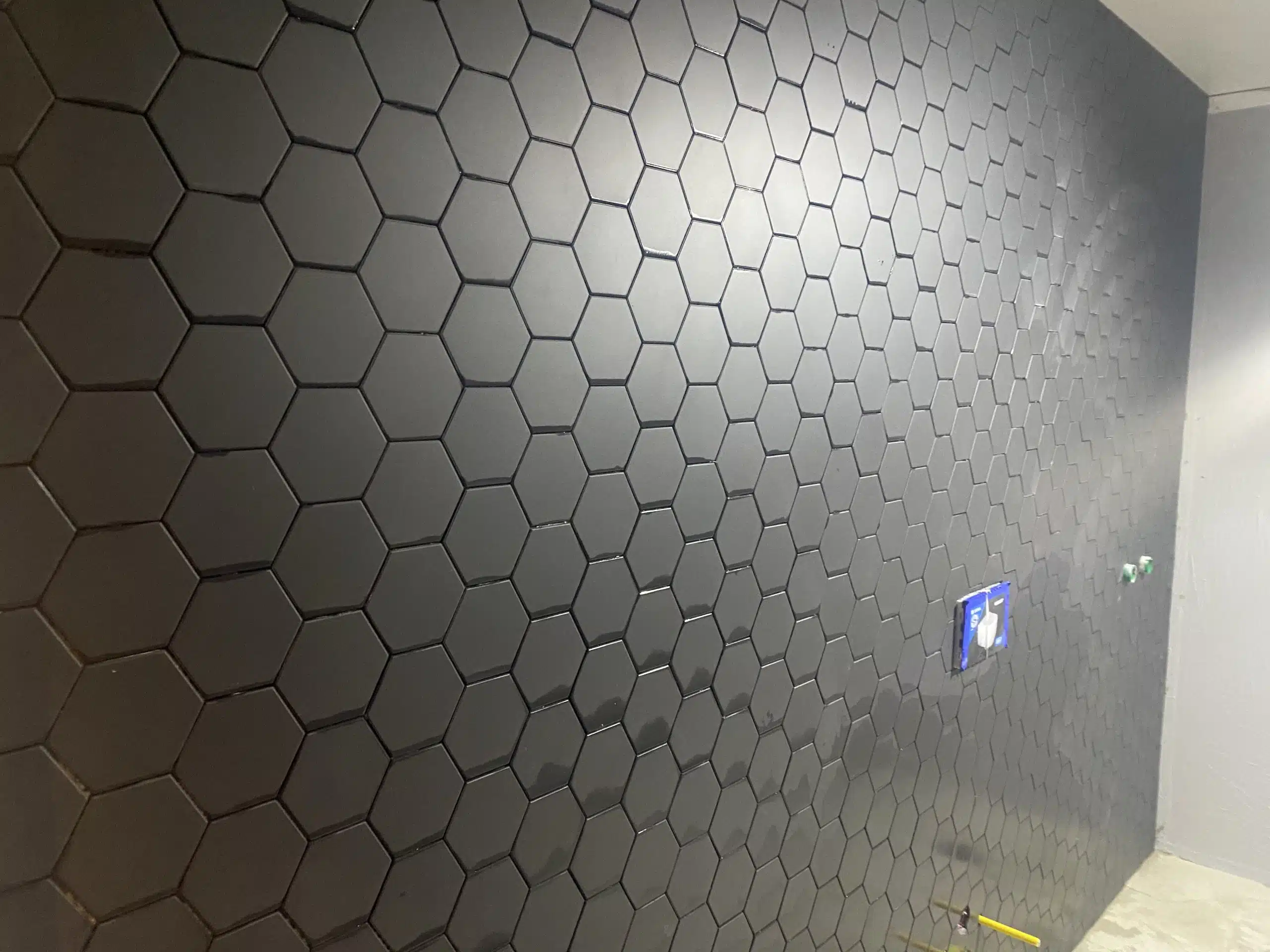 Svart vegg kledd med sekskantede fliser i et rom under oppussing.