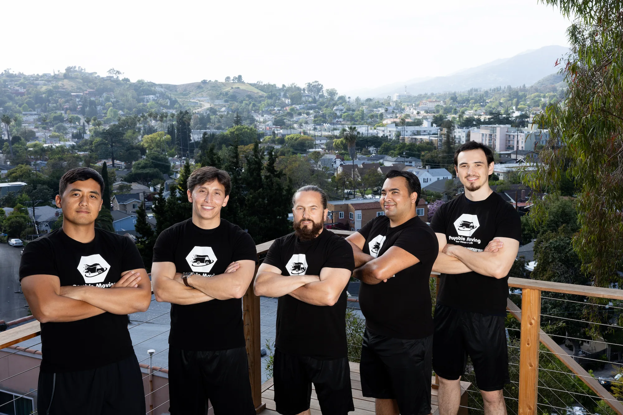 Payable Moving team of five movers standing with folded arms on a balcony overlooking a hillside Los Angeles neighborhood.
