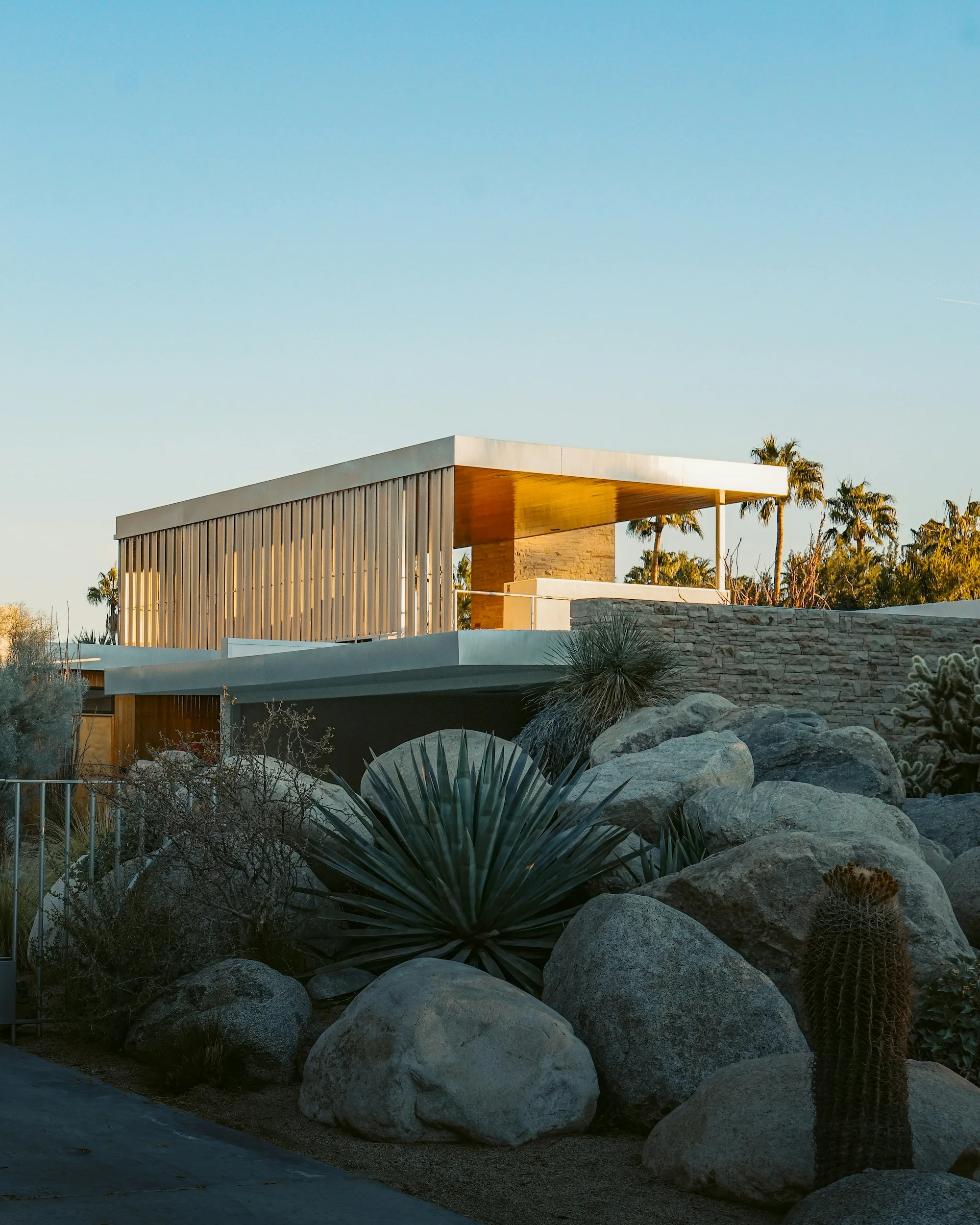Modern desert home with minimalist architecture, large windows, and surrounding cacti and rock landscaping