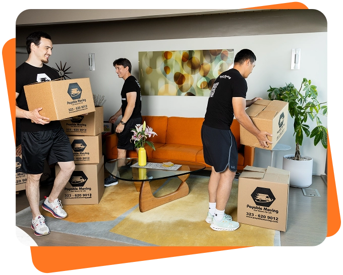 Payable Moving crew carefully carrying and stacking labeled moving boxes inside a bright modern living room.