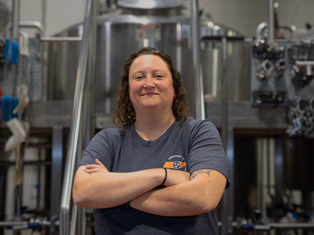 Image of Alisha Dowling, Lead Brewer at Black Abbey brewing standing in front of the brew system.