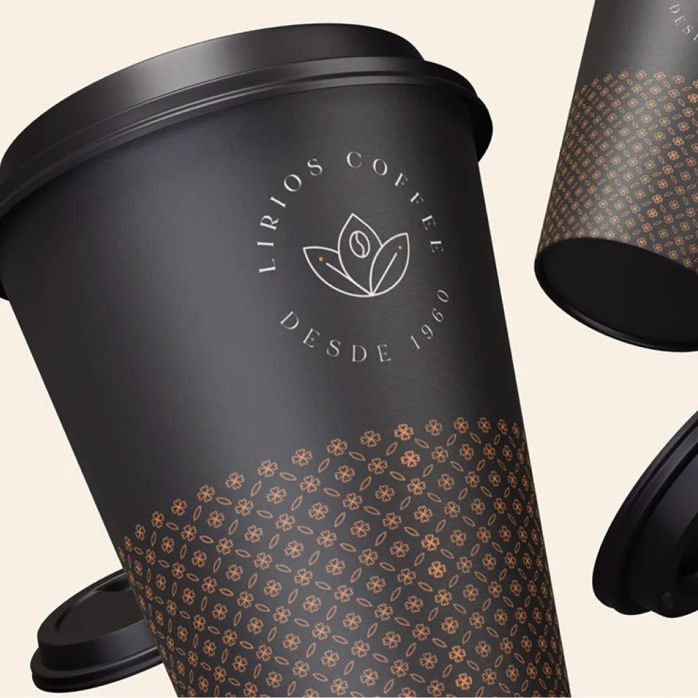 Vaso negro para café con tapa, con patrón de flores pequeñas en dorado y logotipo “Lirios Coffee desde 1960”, manteniendo coherencia con el sistema visual. Servicio de branding, ubicación Perú.