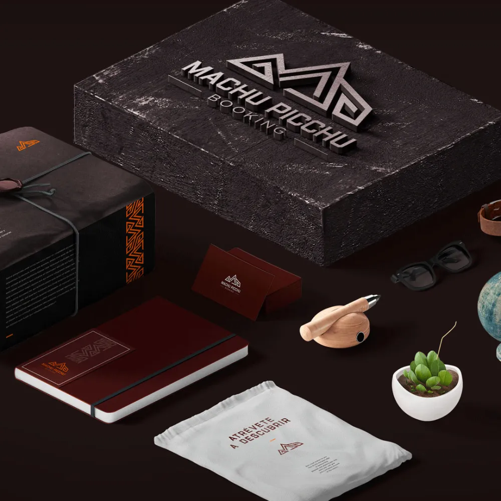 Diseño de branding Machu Picchu con caja negra, cuaderno marrón, bolsa blanca con texto 'Atrévete a descubrir', tarjetas y otros objetos en fondo oscuro. Servicio de branding, ubicación Cusco, Perú.