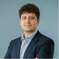 Hombre joven con cabello rizado y traje azul mirando a la cámara con fondo azul claro.