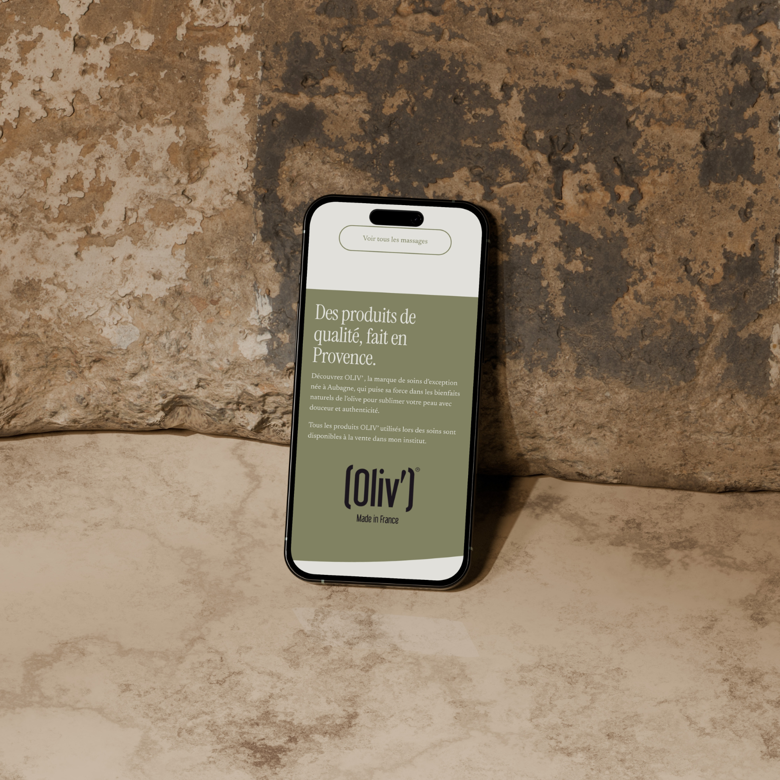 Un smartphone posé contre un mur texturé affiche une page en français sur des produits de soin faits en Provence par la marque Oliv'.