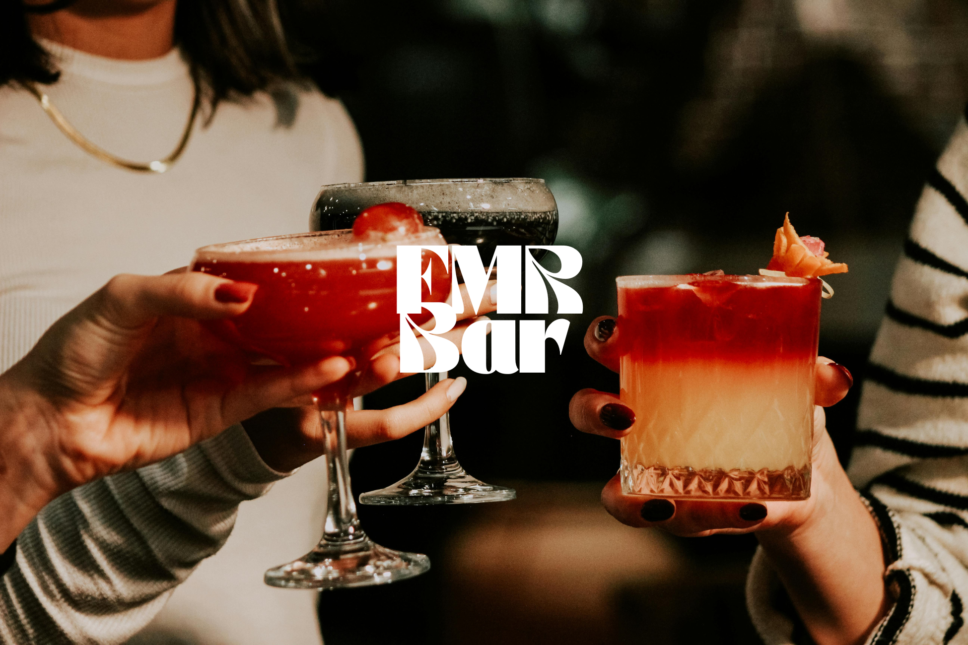 Trois mains tenant des cocktails colorés dans des verres élégants lors d'une soirée.