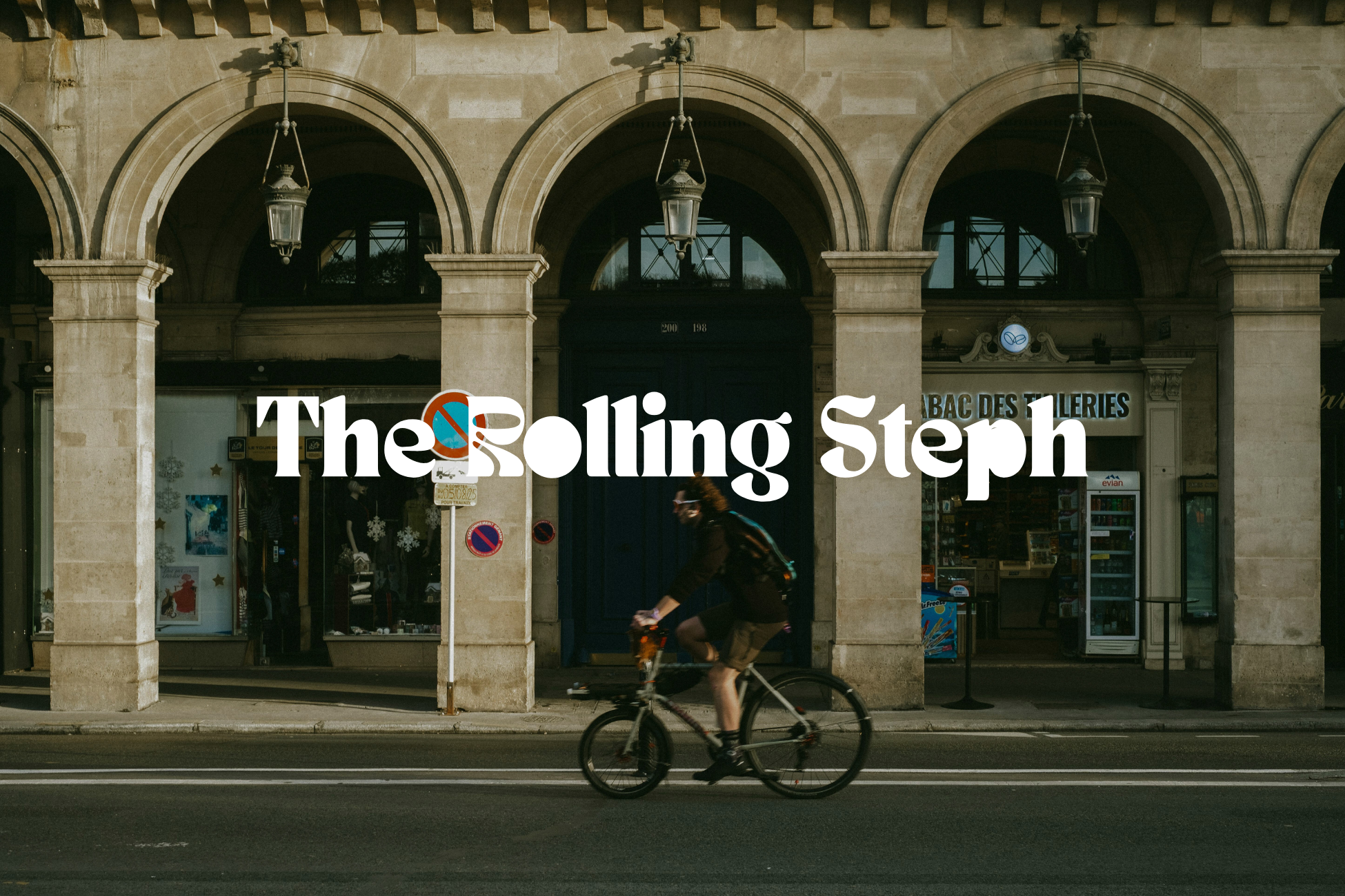 Une personne masquée faisant du vélo sur une rue devant un bâtiment à arcades en pierre avec des lanternes suspendues.