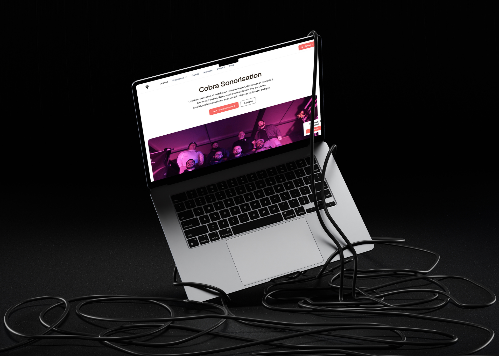 Ordinateur portable affichant la page d'accueil de Cobra Sonorisation avec des câbles noirs enchevêtrés autour.
